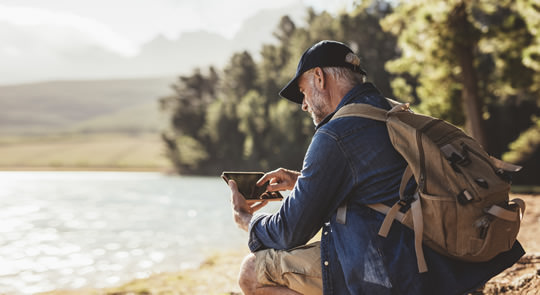 Photo of man using a tablet while hiking by a loch